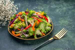 Free photo side view of delicious vegan salad in a plate with various vegetables and fork white flower on dark background