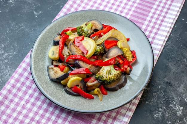 Side view of delicious vegetarian meal on a plate on purple stripped towel on dark background