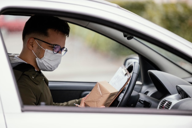 Side view delivery man with mask in car