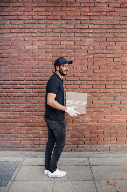 Free photo side view of a delivery man with parcel in front of brickwall