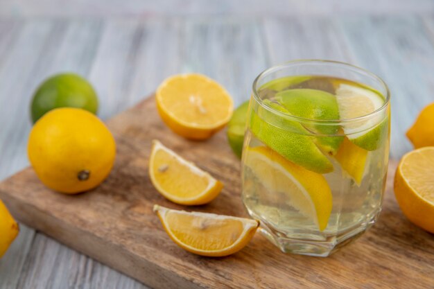 Side view detox water in a glass with lime wedges and half an orange and lemon on a cutting board