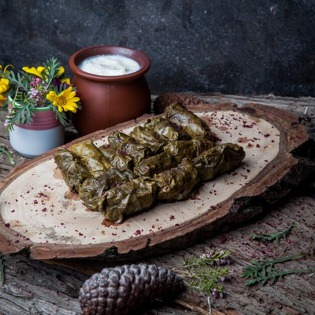 Side view dolma grape leaves stuffed with meat and rice with sour cream sauce on a dark wooden table. eastern european and asian traditional cuisine