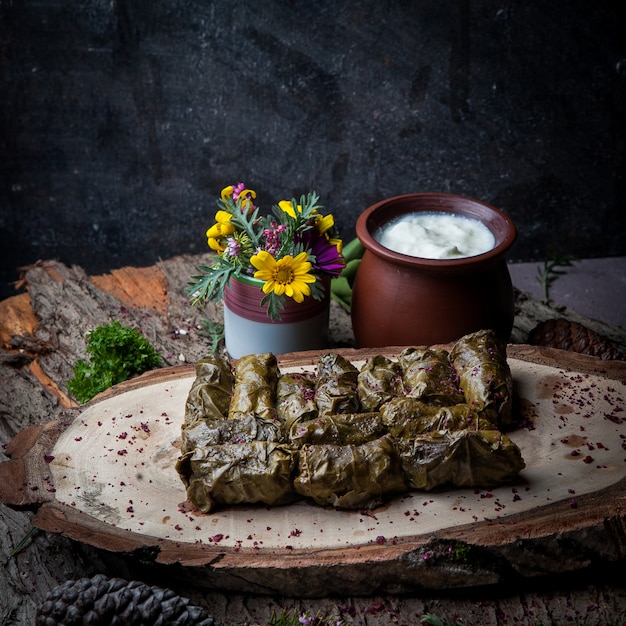 Side view dolma grape leaves stuffed with meat and rice with sour cream sauce on a dark wooden table. eastern european and asian traditional cuisine