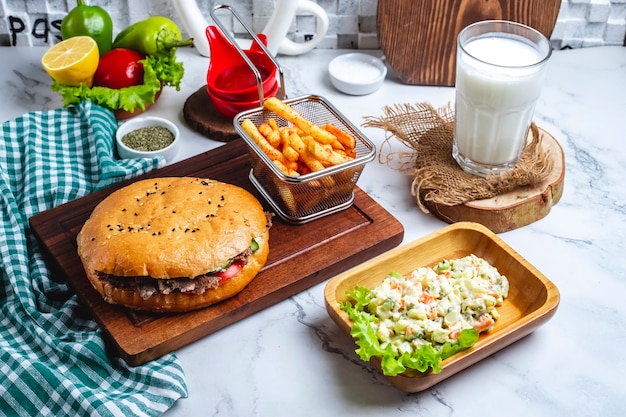 Side view of doner kebab with meat in pita bread on a wooden board with mixed vegetable salad french fries and ayran drink