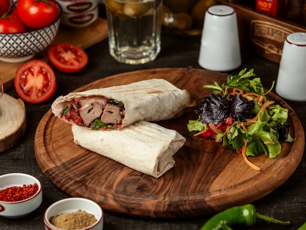 Side view of doner kebab wrapped in lavash with fresh salad on wooden board