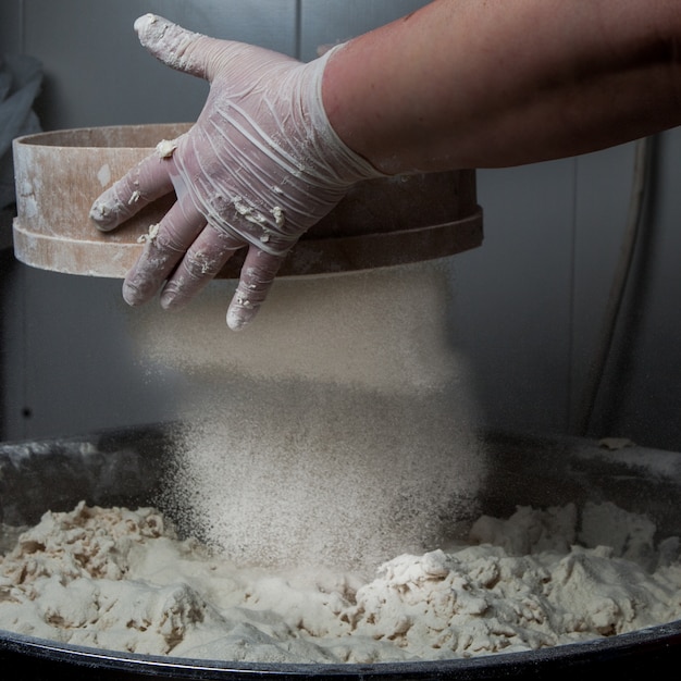 Free photo side view dough with flour and sieve and human hand