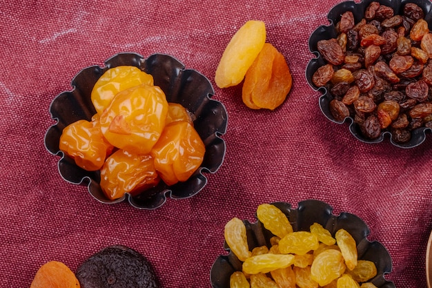 Side view of dried fruits cherry plums raisins and apricots in mini tart tins on sackcloth texture background