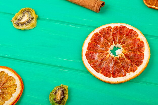 Side view of dried grapefruit and orange slices with cinnamon sticks and dried kiwi slices on green wooden background