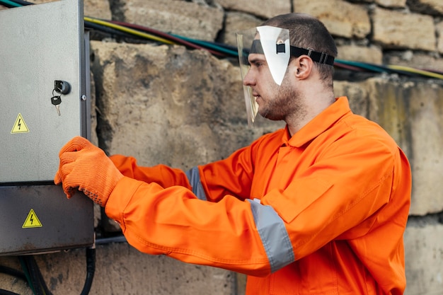 Side view of electrician in uniform with protective gloves and face shield