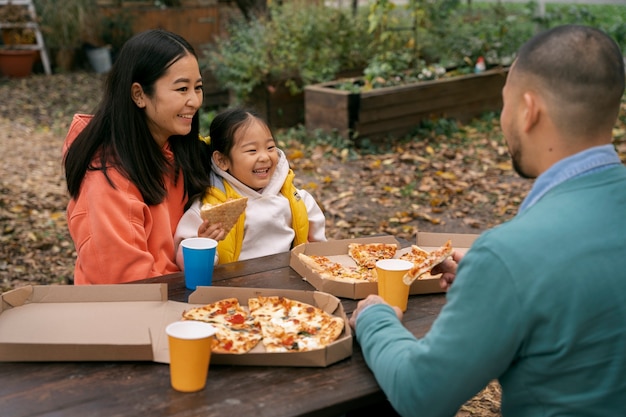 Free photo side view family eating pizza outdoors