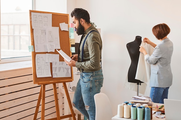 Free photo side view of fashion designers in atelier with dress form and idea board