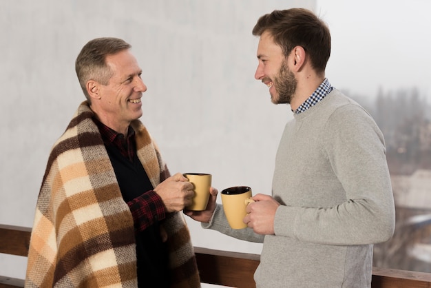 Side view of father and sun smiling and holding cups in hands