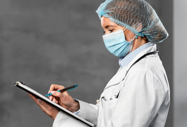 Free Photo side view of female doctor with medical mask and hairnet holding clipboard with copy space