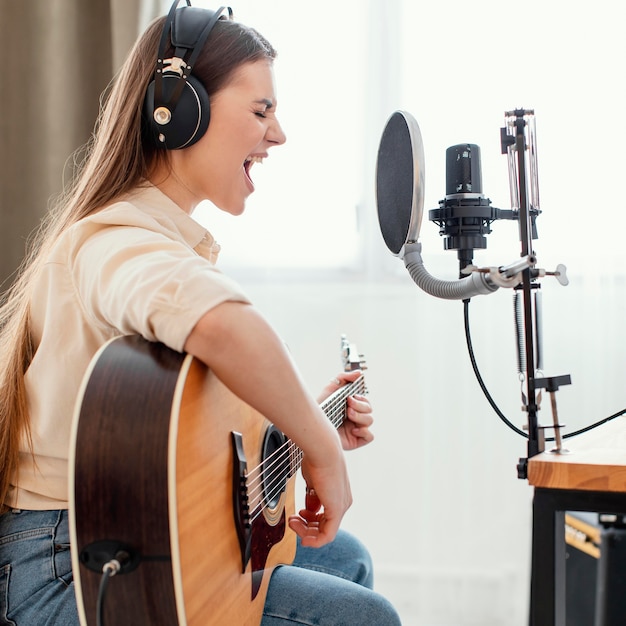 Free photo side view of female musician at home recording song and playing acoustic guitar