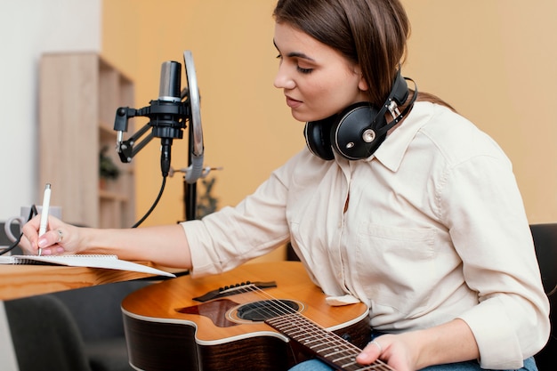 Side view of female musician at home writing song while playing acoustic guitar