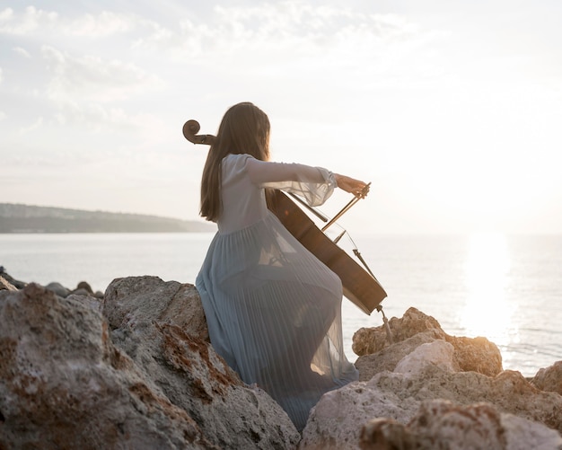 Side view of female musician playing cello at sunset on rocks