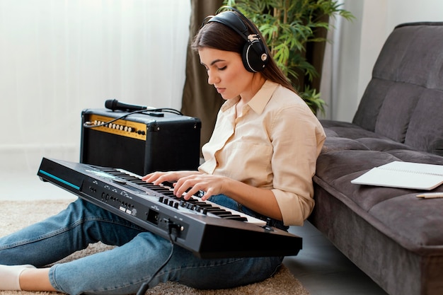 Side view of female musician with headphones playing piano keyboard