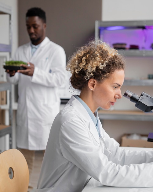 Side view of female researcher in the laboratory with microscope and male colleague