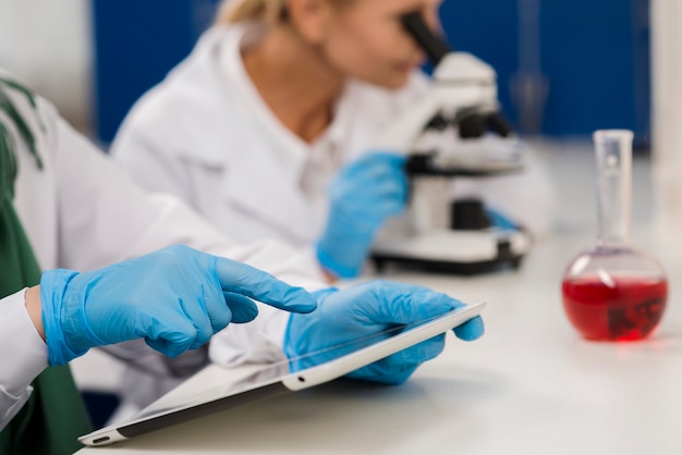 Free photo side view of female scientists in the lab working with microscope and tablet