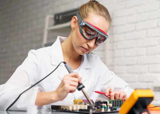 Side view of female technician with soldering iron and electronics motherboard