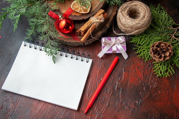 Side view of fir branches and closed spiral notebook with pen cinnamon limes ball of rope on dark table