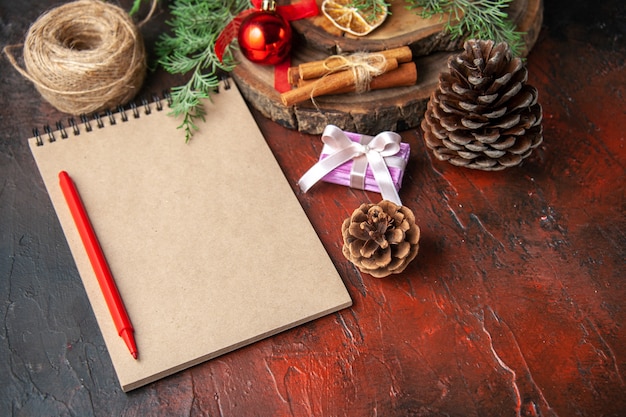 Side view of fir branches and closed spiral notebook with pen cinnamon limes conifer cone and ball of rope on dark background