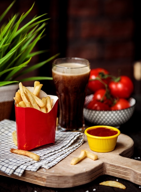 Side view of french fries in cardboard bag with ketchup on wooden cutting board