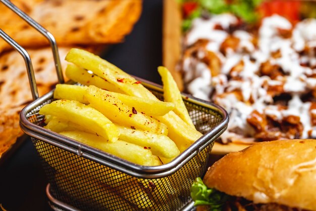 Side view french fries in stainless steel mini basket with salt and burger on the table