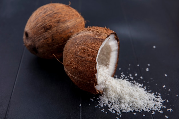 Side view of fresh and brown coconuts with coconut powder on a black surface