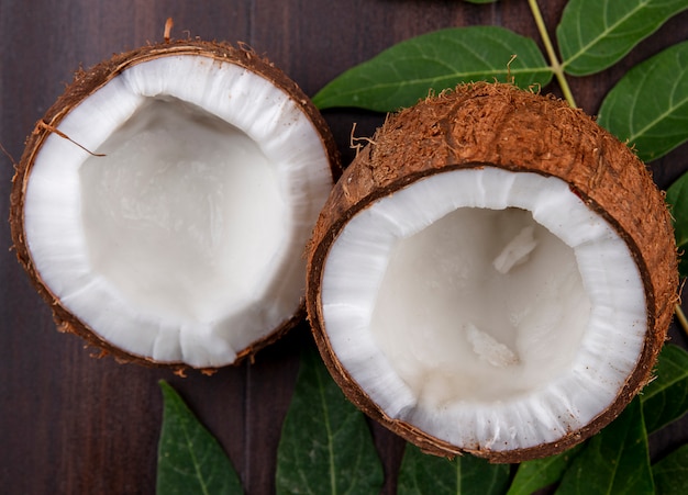 Side view of fresh and brown coconuts with leaf on wooden surface