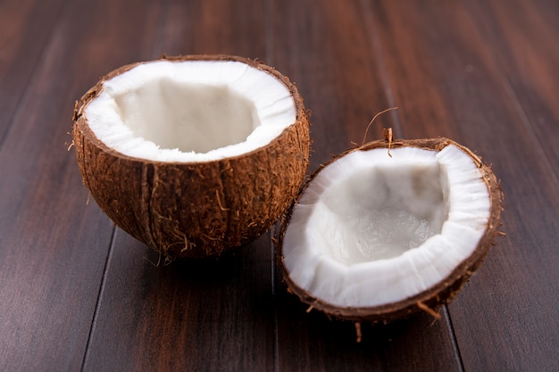 Side view of fresh brown and halved coconuts on a wooden surface