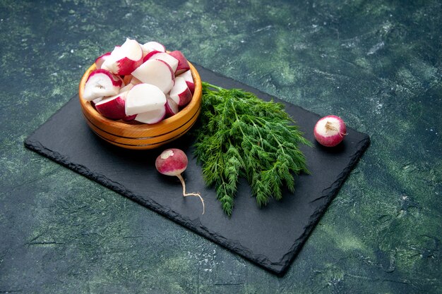 Side view of fresh dill bundle and whole radishes knife on black cutting board on green black mix colors background with free space