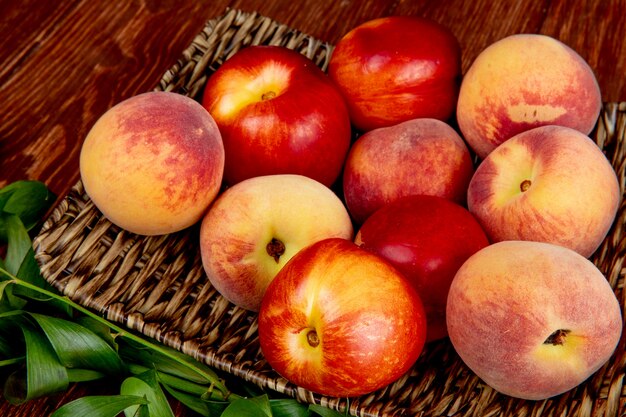 side view of fresh ripe nectarines and peaches on a wicker tray on wooden rustic table