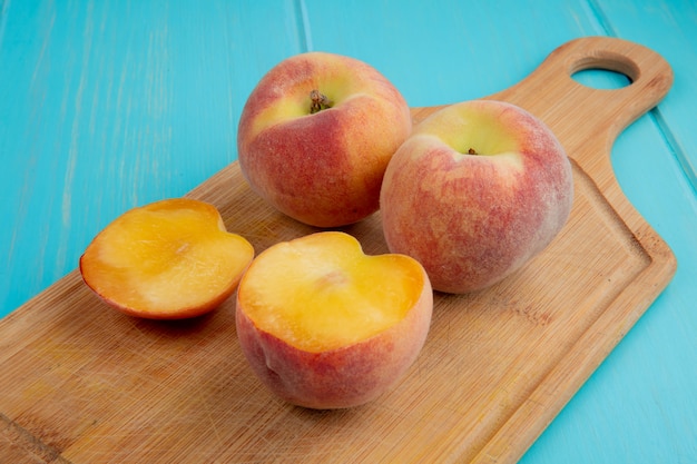 Free photo side view of fresh ripe peaches on a wood cutting board on blue