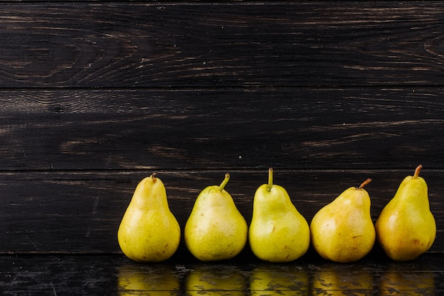 Free photo side view of fresh ripe pears in a line on black wooden background with copy space