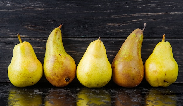 Side view of fresh ripe pears in a line on black wooden background