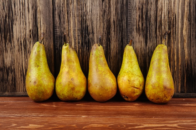 Side view of fresh ripe pears in a line on a wooden background