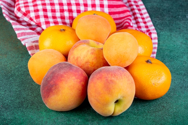 Free photo side view of fresh ripe sweet peaches and tangerines on plaid fabric on dark