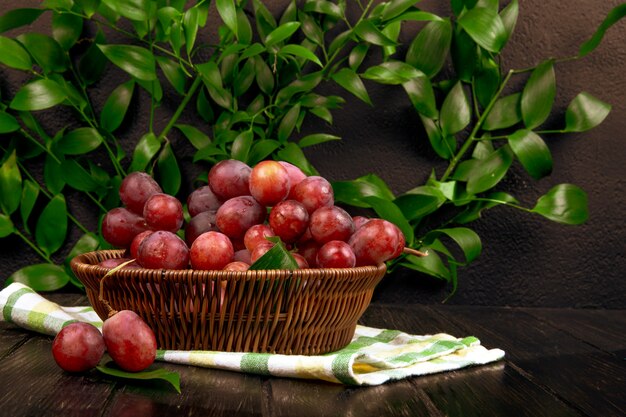 Side view of fresh sweet grape in a wicker basket on wooden surface on green leaves table