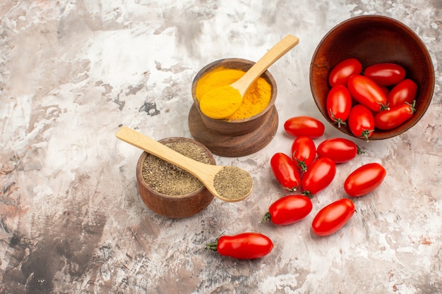 Side view of fresh tomatoes fallen from a small pot and various spices on gray background