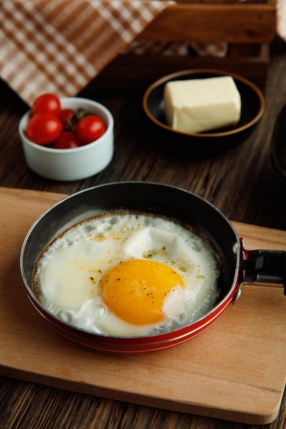 Free photo side view of fried egg in frying pan on cutting board with tomatoes butter on wooden background