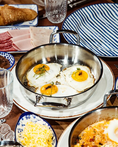 Side view of fried eggs in a pan on wooden table