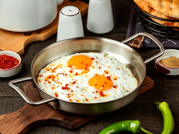 Free photo side view of fried eggs with red spices in a pan on wooden board