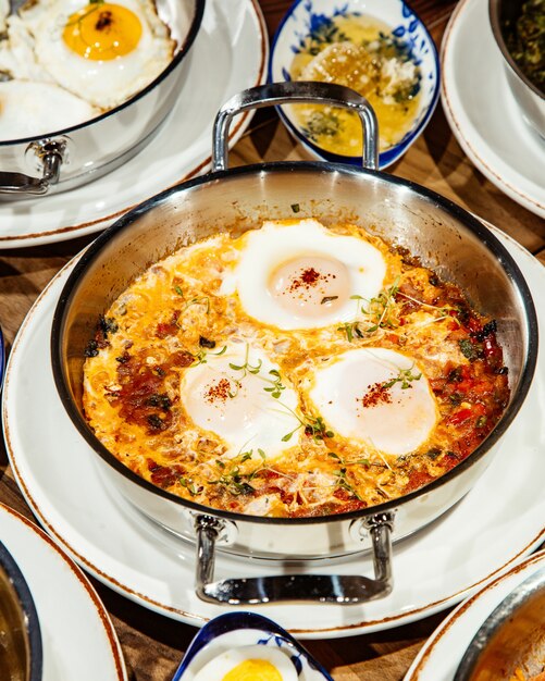 Side view of fried eggs with tomatoes onionnd chicken in a pan