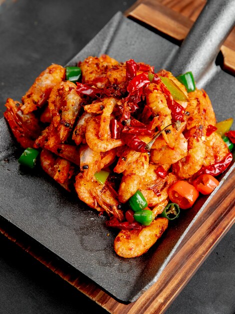 Side view of fried shrimps with red and green peppers on a wooden cutting board