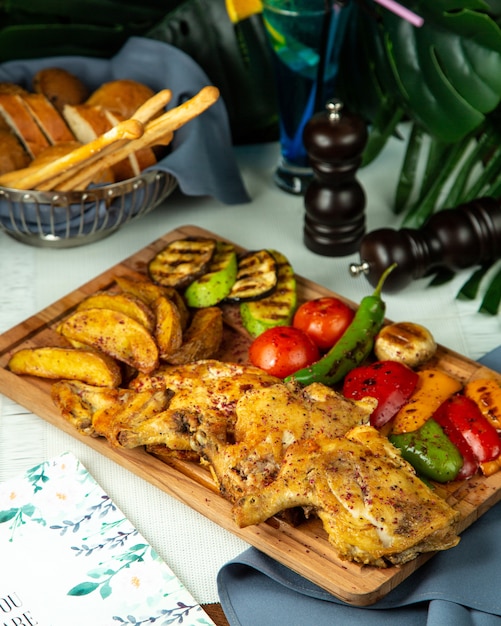 Side view fried tobacco chicken with potatoes and grilled vegetables on a wooden board