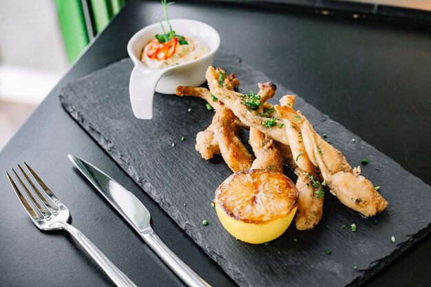 Side view frog legs in batter with sauce and lemon on a tray