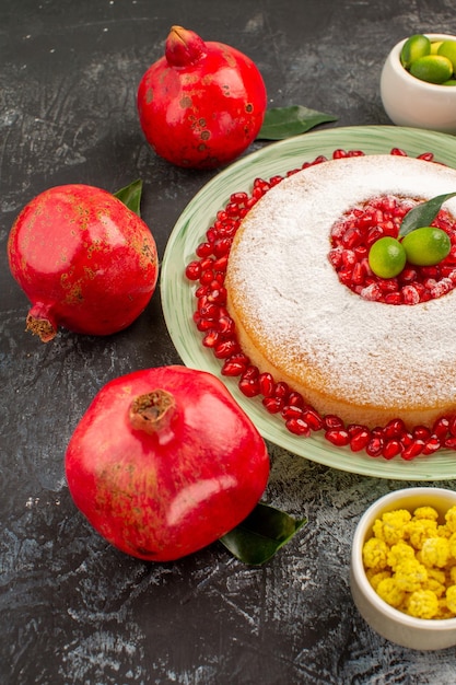 Side view from afar cake sweets an appetizing cake yellow candies limes and three red pomegranate