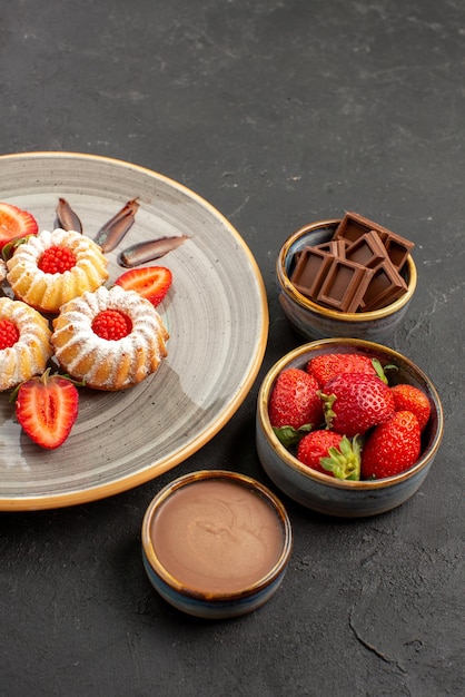 Side view from afar chocolate and cookies bowls of chocolate strawberries and chocolate cream next to the plate of cookies with strawberries on table