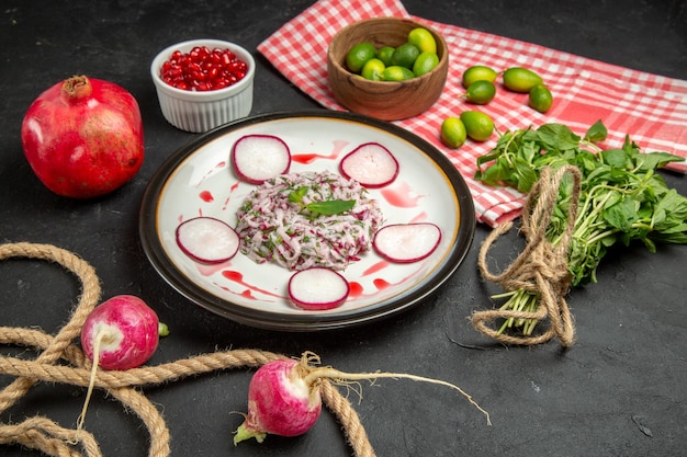 Free photo side view from afar a dish a dish of redish greens rope pomegranate citrus fruits